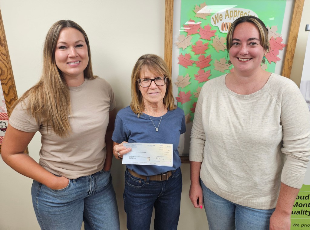 Three representatives pose with a $1,078 Roosevelt County Community Foundation grant check for a new medical-grade chair at the NEMHS Poplar Laboratory.
