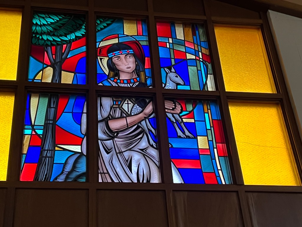 Saint Kateri Tekakwitha depicted with a deer and trees in a stained-glass window at Our Lady of Lourdes Church in Poplar.