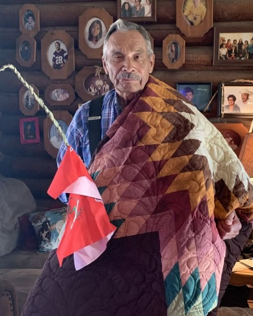 A.T. “Rusty” Stafne wrapped in a star quilt and holding a braid of sweetgrass adorned with red and white cloth.