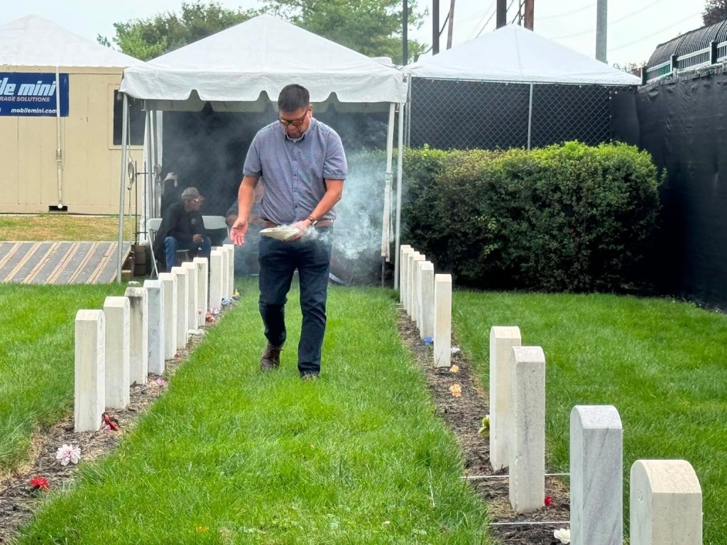 Melvin Scott smudging between rows of graves at Carlisle Indian Cemetery