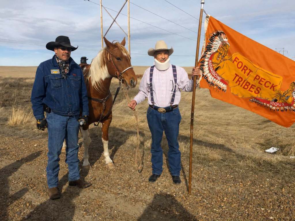 Former Fort Peck Tribal Chairman A.T. “Rusty” Stafne stands with his son Grant Stafne, a horse and an orange Fort Peck Tribal Flag.