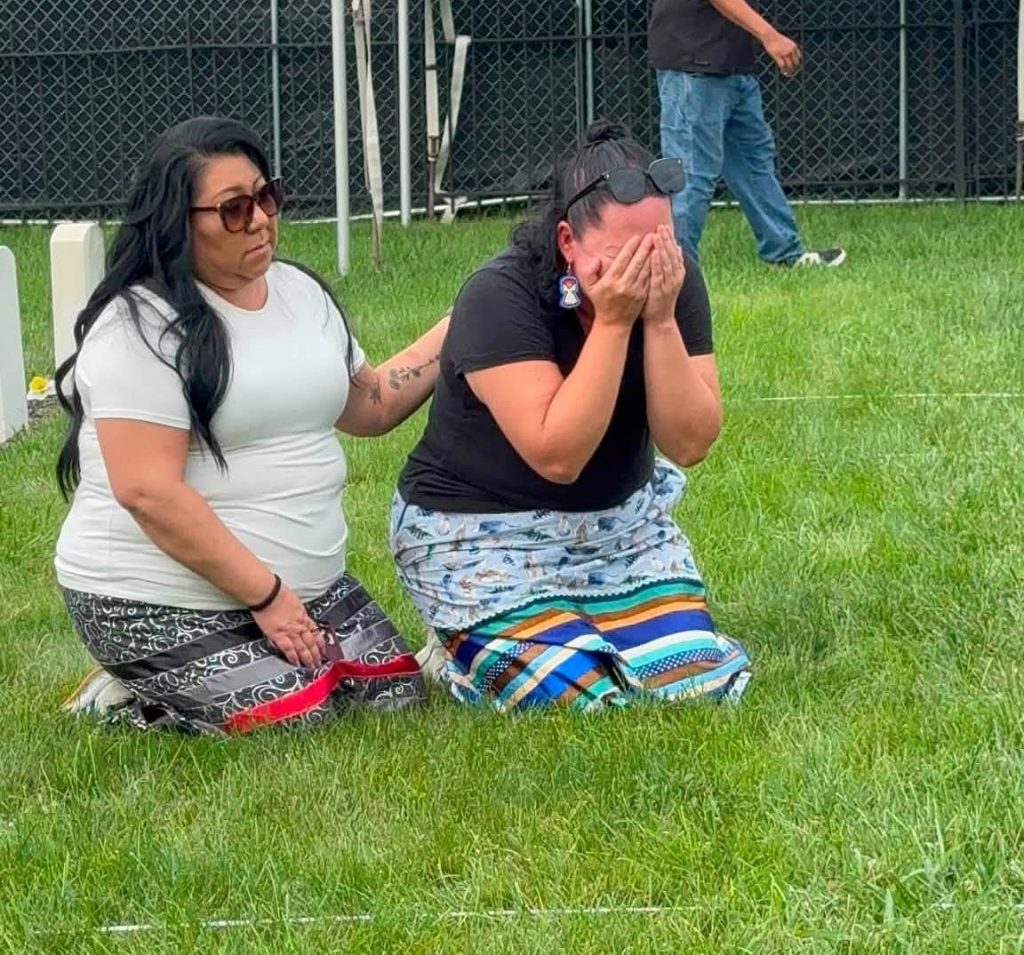 Michael Redstone kneeling and crying as Shaye Frank comforts her at Carlisle Indian Cemetery