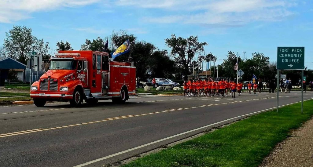 The Poplar Volunteer Fire Department’s orange fire engine drives along the road with orange-shirted runners and other procession participants following behind.