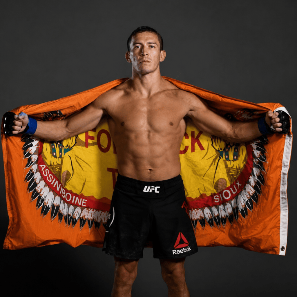 Fort Peck fighter Hunter Azure stands with an orange Fort Peck Tribal Flag behind him.