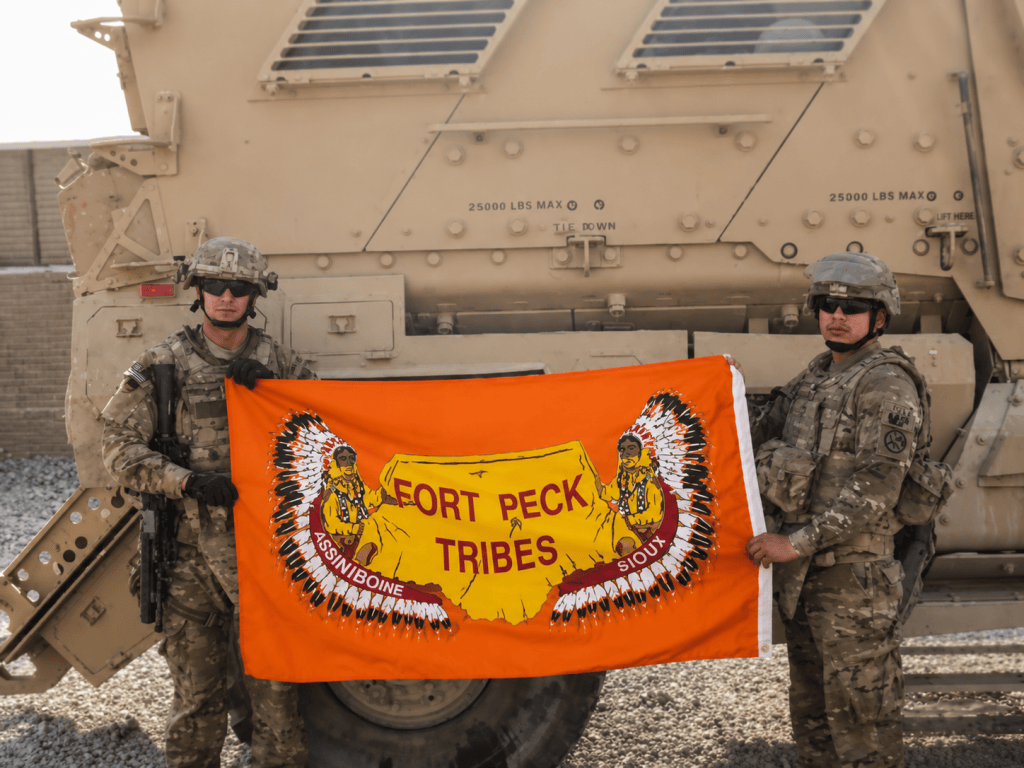 Ryan Michaelsen and Jesse Falcon hold an orange Fort Peck Tribal Flag while serving in Afghanistan.
