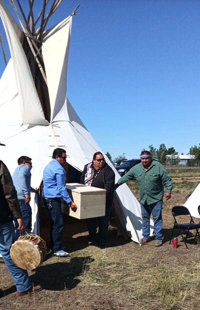 Several men carry a wooden burial box from a tipi during the graveside services for Peter Howe and Richard Morgan.